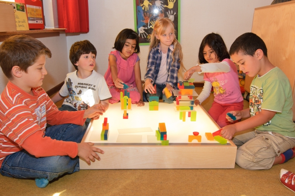 Auf dem Leuchttisch sehen die bunten Steine und Türme besonders schön aus. Die Kinder haben auf einen Tisch mit Beleuchtung verschiedene Konstruktionen gebaut. Nun schauen sie sich diese gena