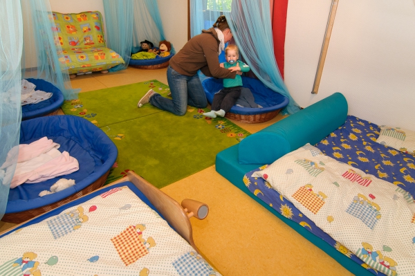Jedes Kind hat seinen Platz. Eine Erzieherin legt ein Kind zum Schlafen in ein Nestchen hinein.