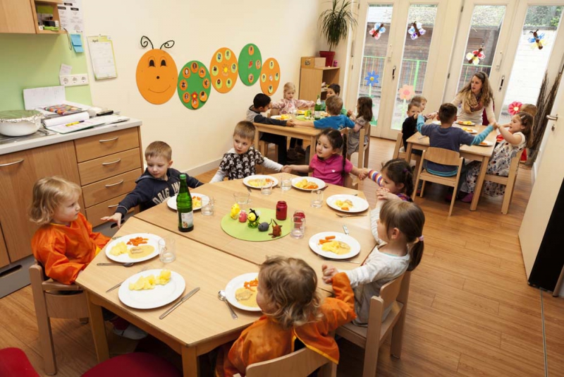 Kinder decken ihren Mittagstisch in der Gruppe und sitzen dort zum gemeinsamen Essen.