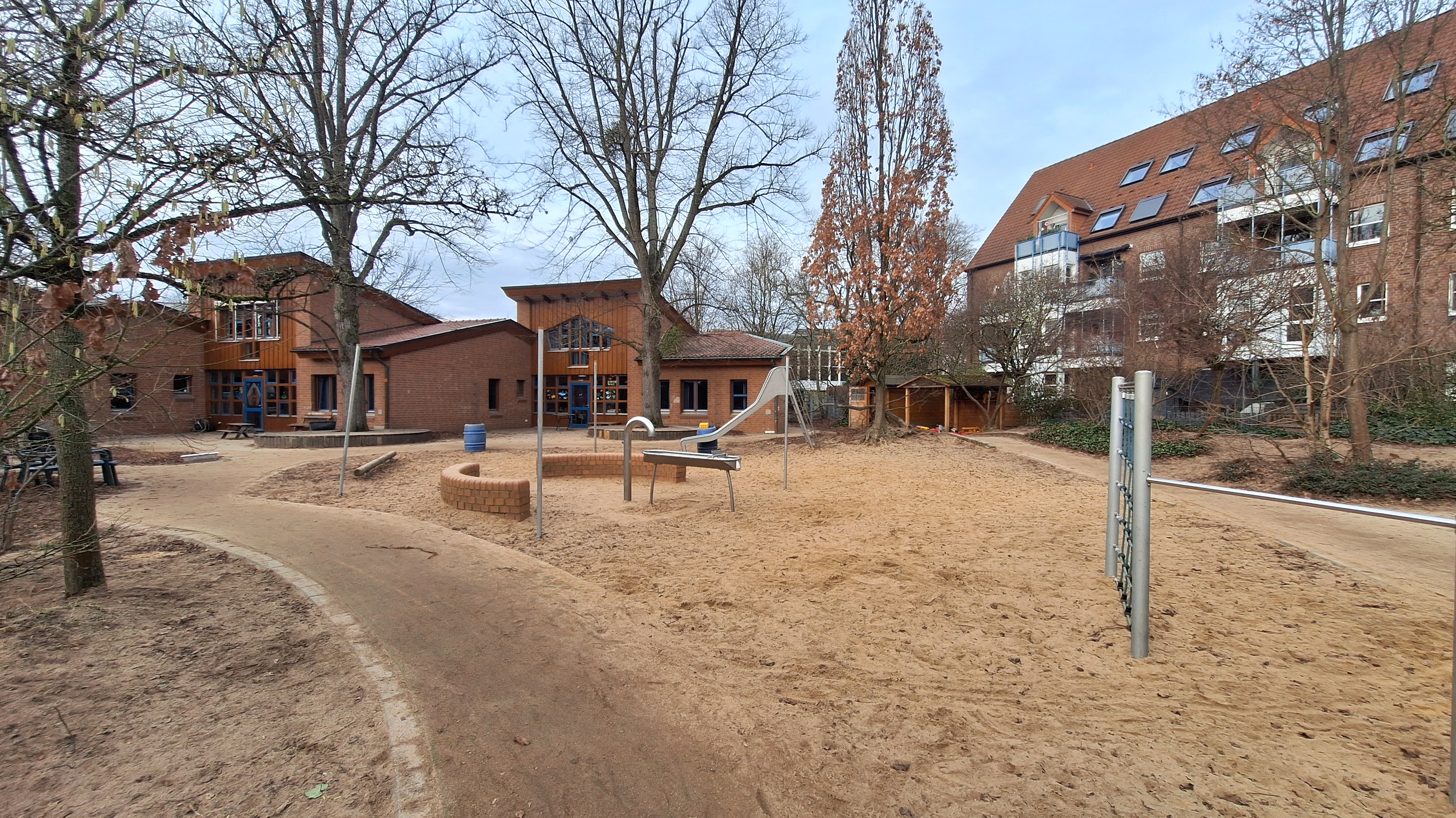 Auf dem Foto sieht man einen Teil des Sandkastens mit Rutsche und Matschanlage sowie die Eingänge zu zwei Gruppenräumen.