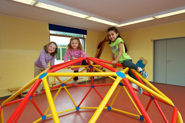Drei Mädchen turnen auf einem Klettergerüst in der Turnhalle, das die Form eines Iglus hat