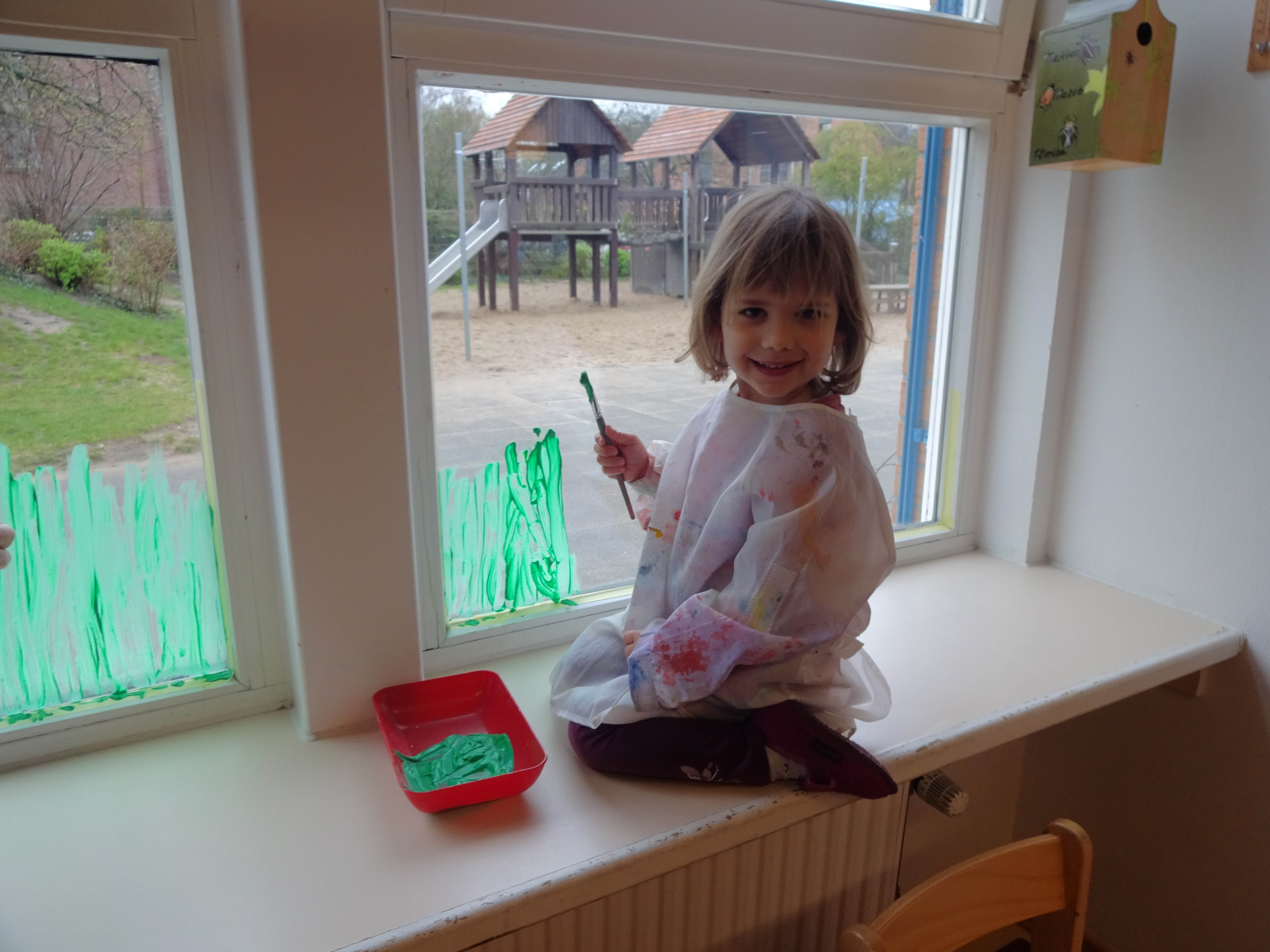 Ein Kind kniet auf der Fensterbank und bemalt die Fenster mit Fingerfarbe