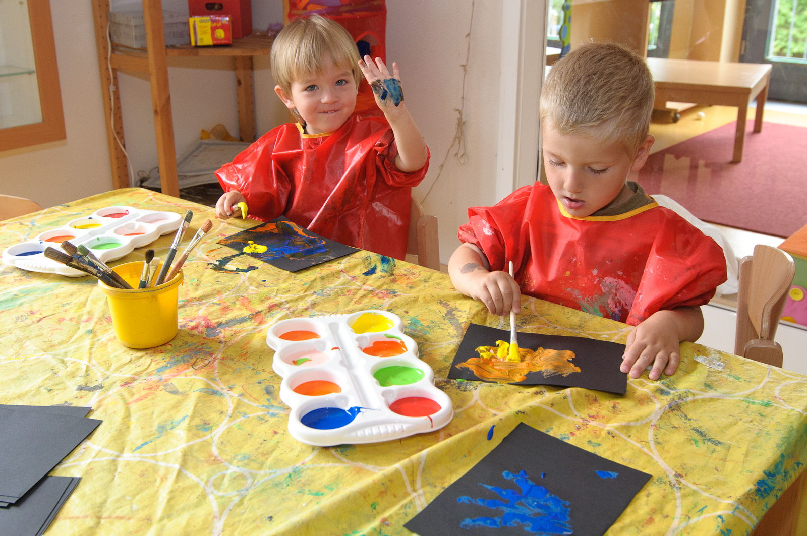Zwei Kinder malen an einem Tisch mit Wasserfarben.