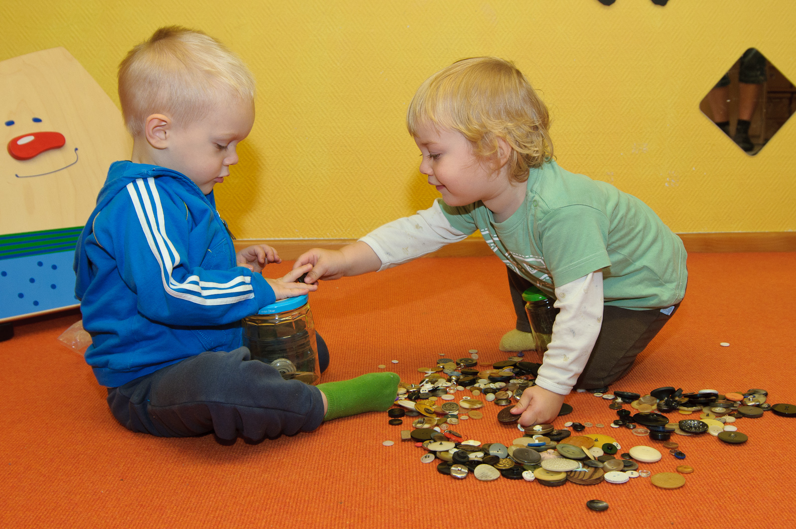 Zwei Kinder sitzen sich gegenüber, entdecken und sortieren unterschiedliche Knöpfe.