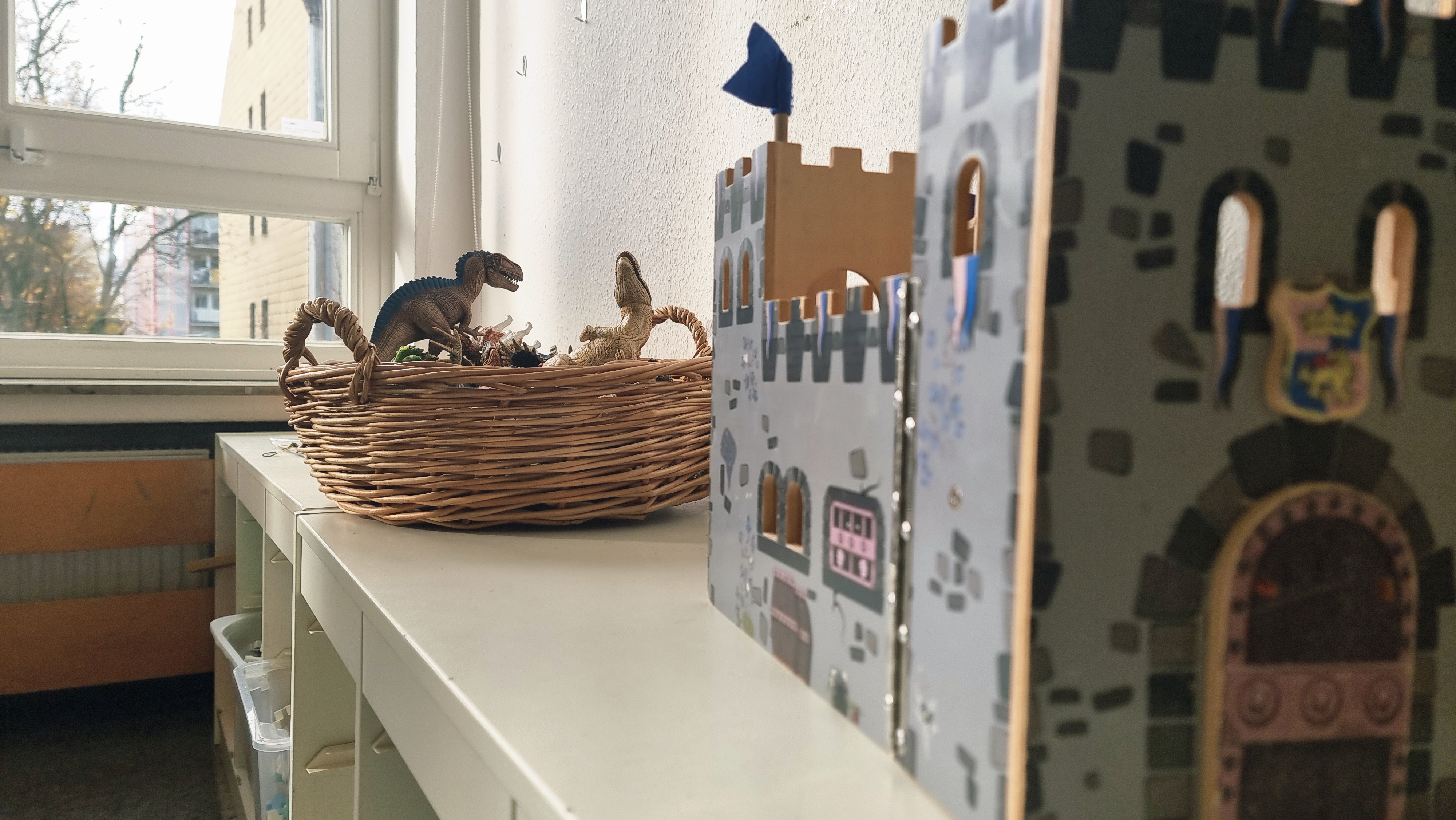 Hier sind verschiedene Spielmaterialien des Bauraums, wie eine Holzritterburg und verschiedene Dinosaurier / Tiere zu sehen.
