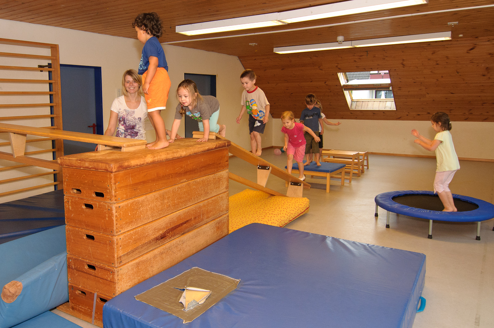 Kinder klettern im Turnraum auf einen Kasten und springen auf eine Matte.